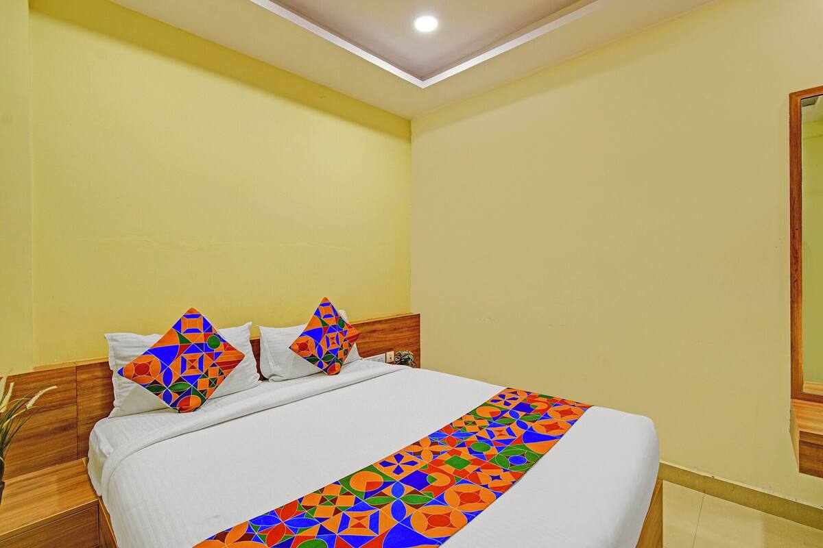 Une chambre d’hôtel avec un lit, une tête de lit en bois, un luminaire au plafond et un miroir sur le mur.