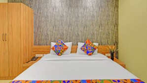 Une chambre d’hôtel avec un grand lit, deux oreillers à motifs géométriques, une armoire en bois et un mur à texture.