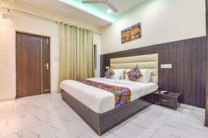 A hotel room with a bed, a nightstand, a ceiling fan, and a painting on the wall. - FabHotel Jugnu (Kharar)