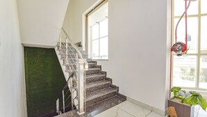 A staircase with a metal railing, a window with a view, and a red fire hose on the wall. - FabHotel Jugnu (Kharar)