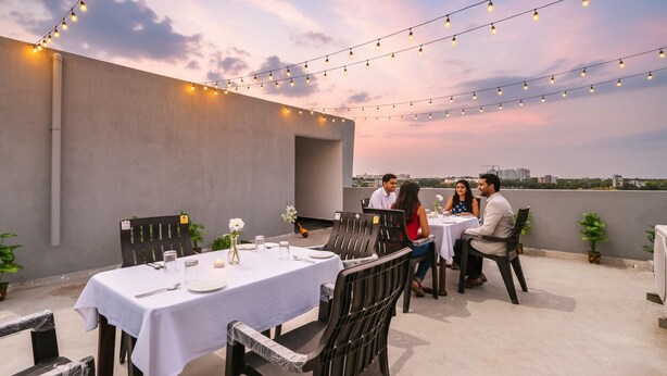 An outdoor dining area with tables and chairs, string lights, and a city view. - FabHotel VK’s Bahadurpally- Nr. Mahindra University, Bahadurpally, Jeedimetla (Hyderabad)