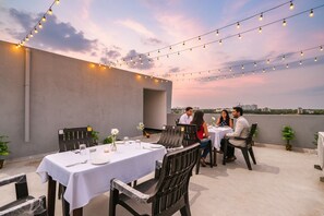 An outdoor dining area with tables and chairs, string lights, and a city view. - FabHotel VKâ€™s Bahadurpally (Hyderabad)