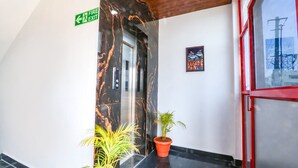 A modern lobby with a marble wall, a fire exit sign, a potted plant, and a framed artwork. - FabHotel VK’s Bahadurpally- Nr. Mahindra University, Bahadurpally, Jeedimetla (Hyderabad)