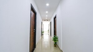 A corridor with white walls, wooden doors, and potted plants. - FabHotel VK’s Bahadurpally- Nr. Mahindra University, Bahadurpally, Jeedimetla (Hyderabad)