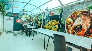 A restaurant with a glass ceiling, tables, chairs, and a menu board. - FabExpress Fen Breeze (Chennai)