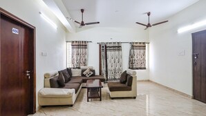 A spacious living room with a sectional sofa, two armchairs, a coffee table, and a ceiling fan. - FabExpress Fen Breeze (Chennai)