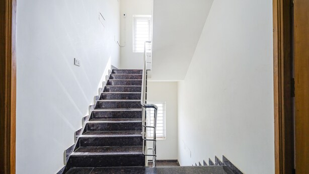 A staircase with dark marble steps and a metal handrail, leading to a landing with a window. - FabExpress Fen Breeze (Chennai)