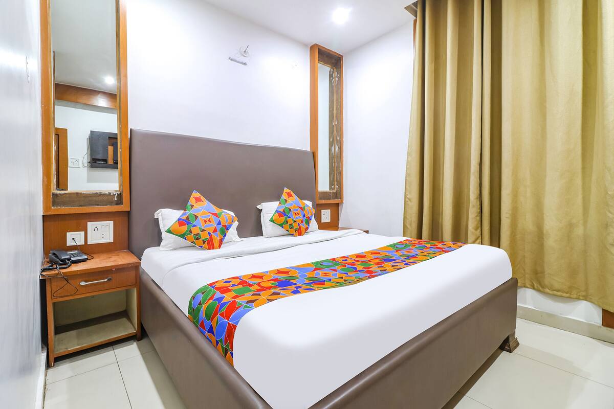 A neatly made bed with a colorful bedspread, a wooden nightstand with a phone, and a mirror on the wall.