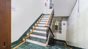 A staircase with marble steps and wooden handrails, leading to a landing with a window and a fire extinguisher. - FabHotel Nand (Patna)