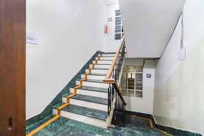 A staircase with marble steps and wooden handrails, leading to a landing with a window and a fire extinguisher. - FabHotel Nand (Patna)