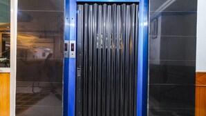 A blue elevator with a metallic door and a control panel on the left side. - FabHotel Nand (Patna)