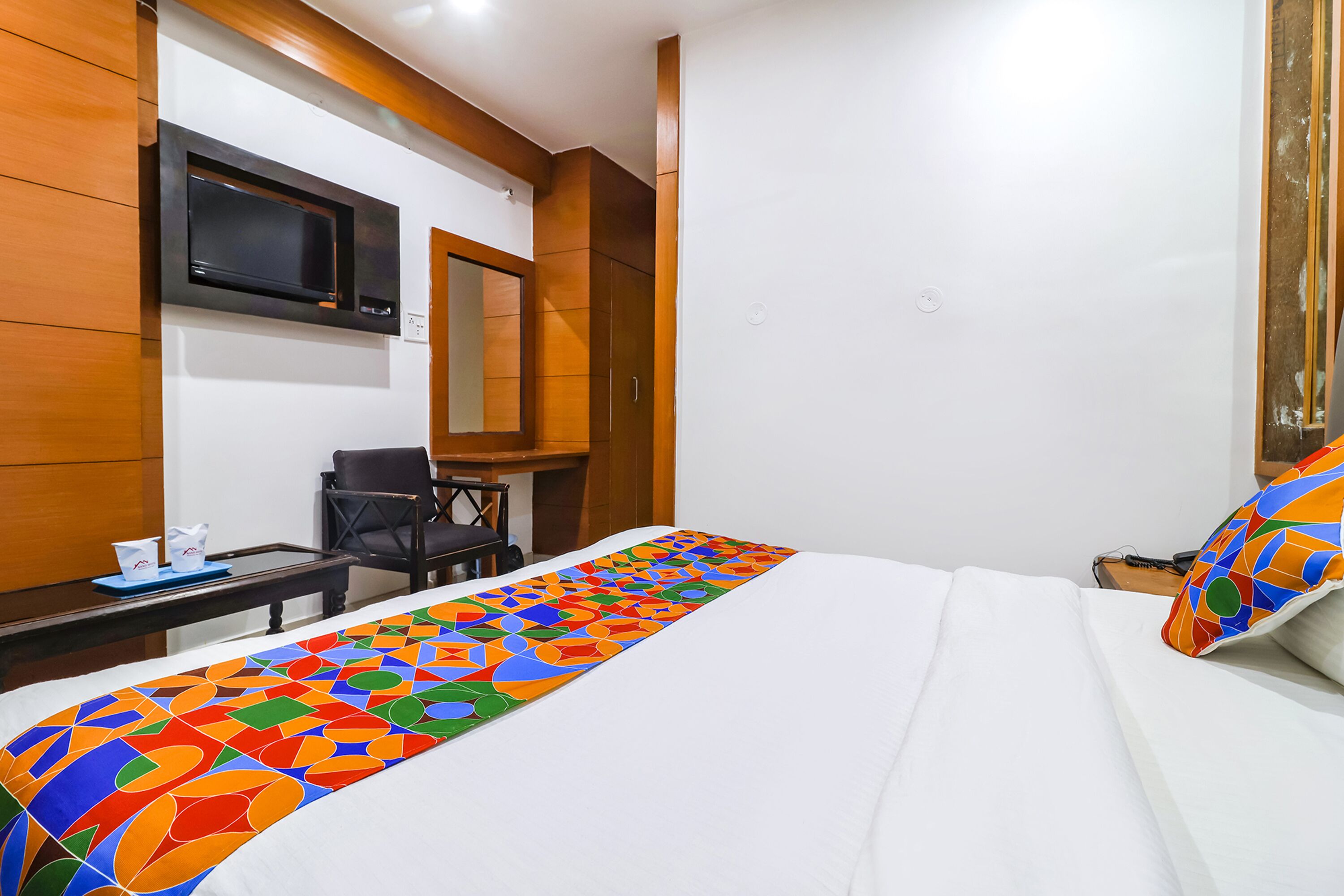 Une chambre d’hôtel comprenant un lit, un bureau, une chaise, un téléviseur fixé au mur et un couvre-lit aux couleurs vives.