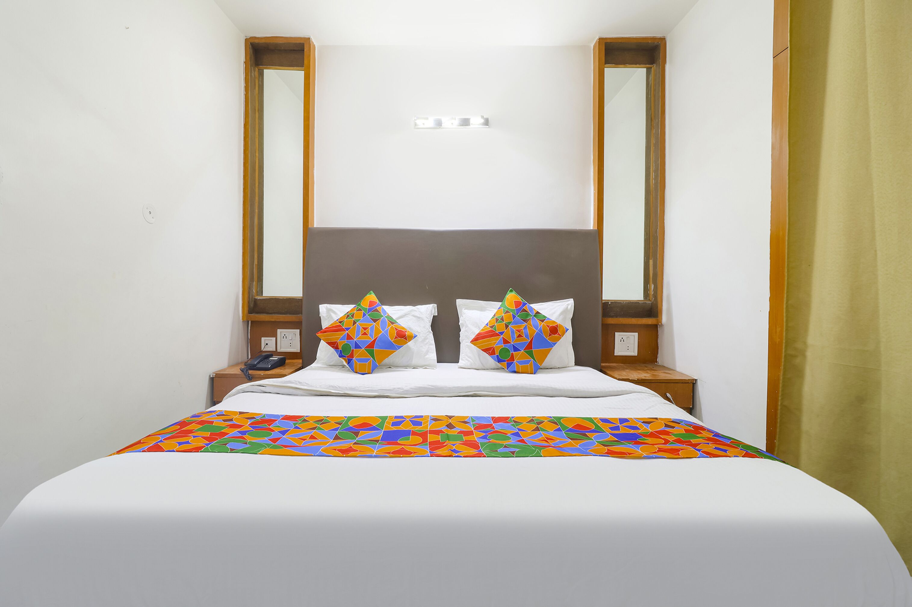 Habitación de hotel con cama, dos mesitas de noche, un espejo y una ventana con cortina.
