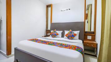 Una cama bien hecha con una colcha colorida, una mesita de noche con una lámpara y un espejo en la pared.