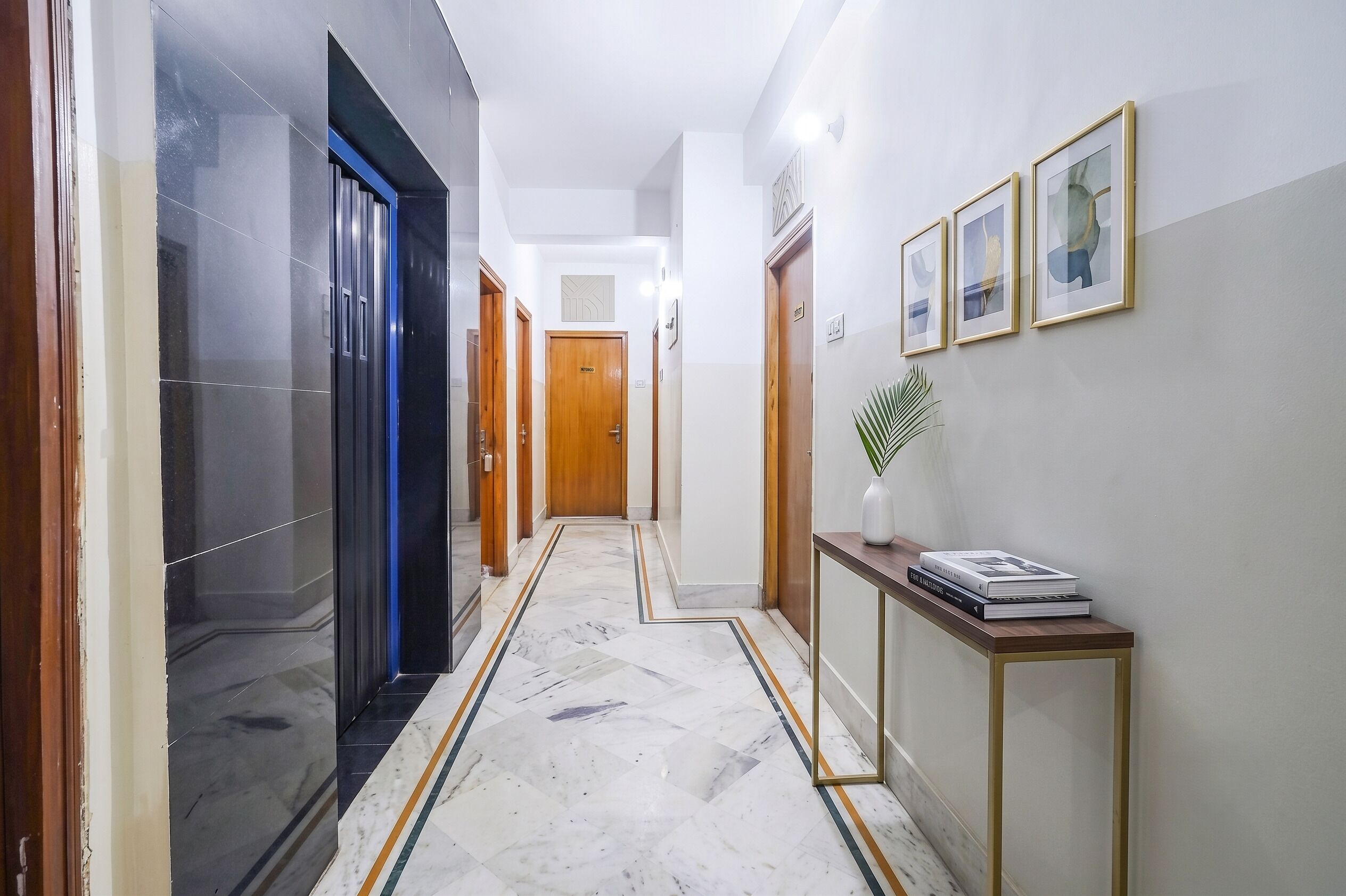 A hallway with a marble floor, wooden doors, and framed artwork on the wall.