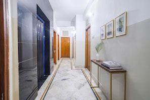 A hallway with a marble floor, wooden doors, and framed artwork on the wall. - FabHotel Nand (Patna)