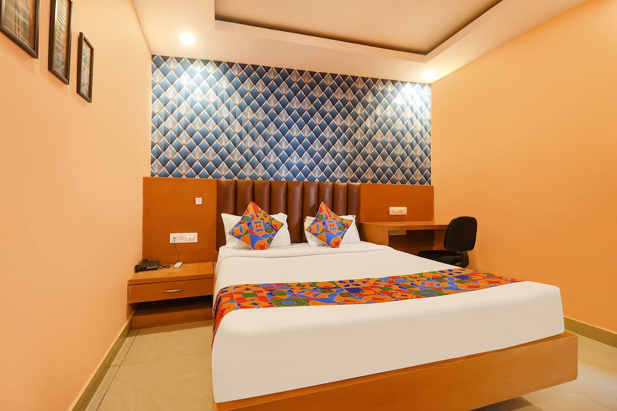 Una habitación de hotel con una cama grande, un cabecero con diseño geométrico, un escritorio con una silla y una mesita de noche con un teléfono y una lámpara.