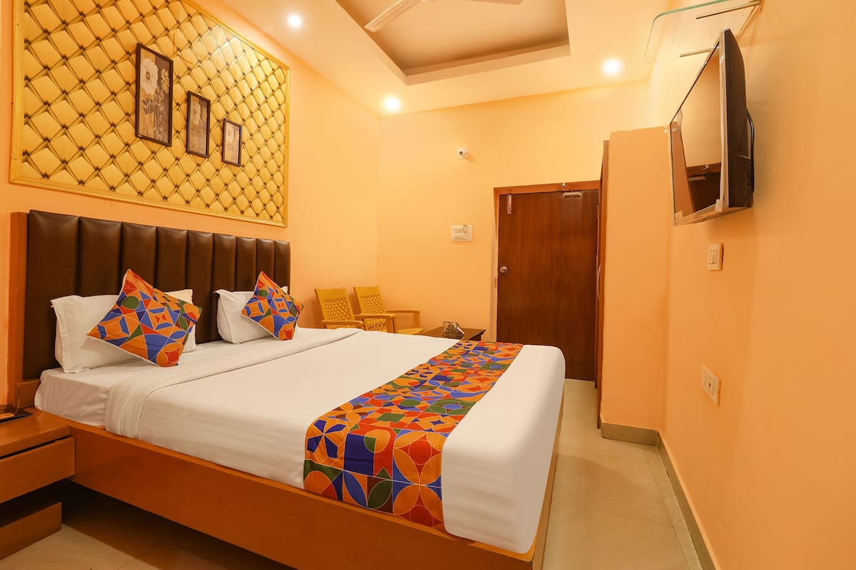 Una habitación de hotel con una cama, un televisor montado en la pared y una puerta que da a otra habitación.