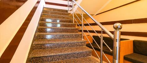 A staircase with granite steps, metal handrails, and a wooden wall panel.