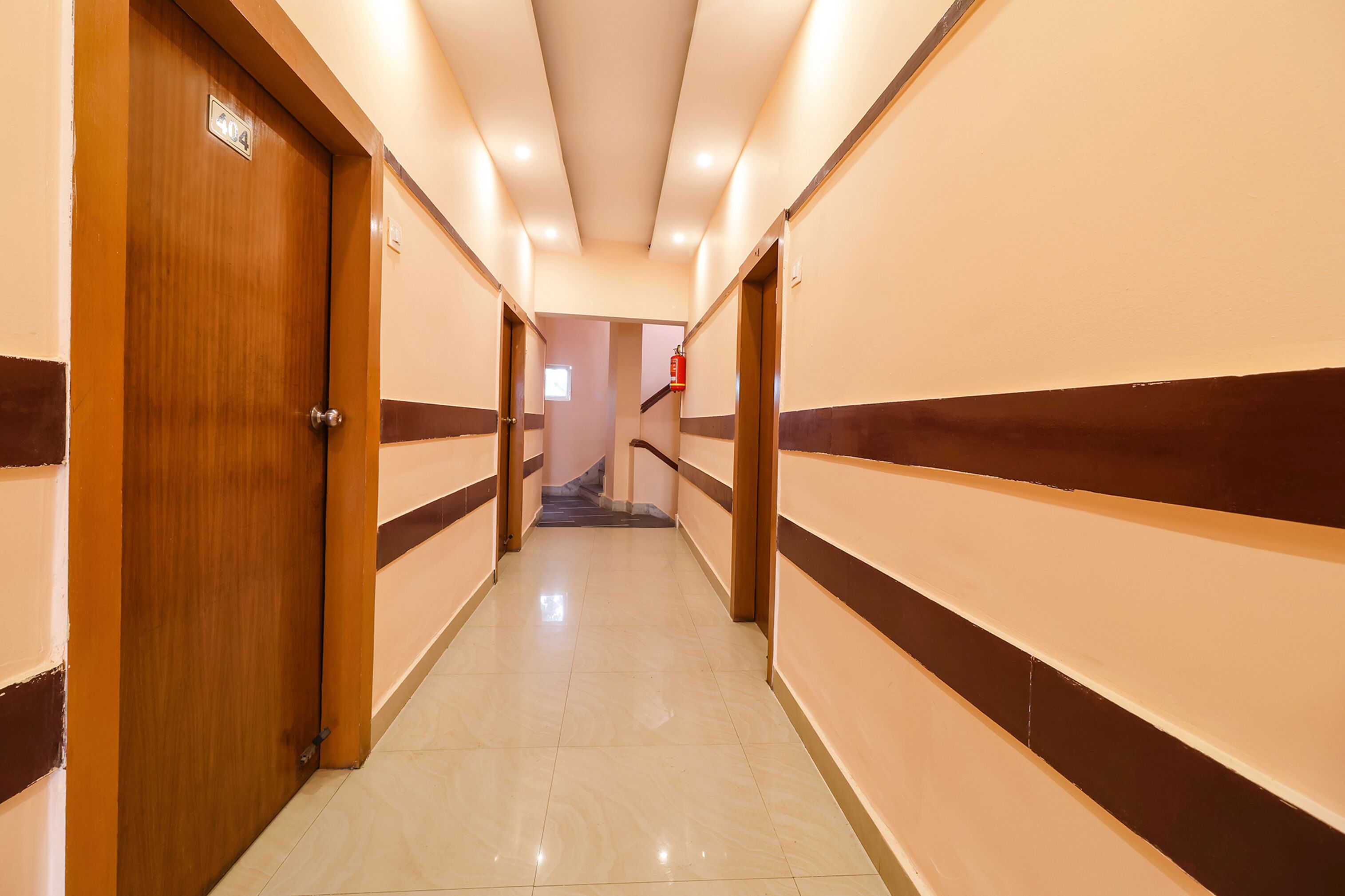 Corridoio di un hotel con porte in legno, un estintore e una scala in lontananza.