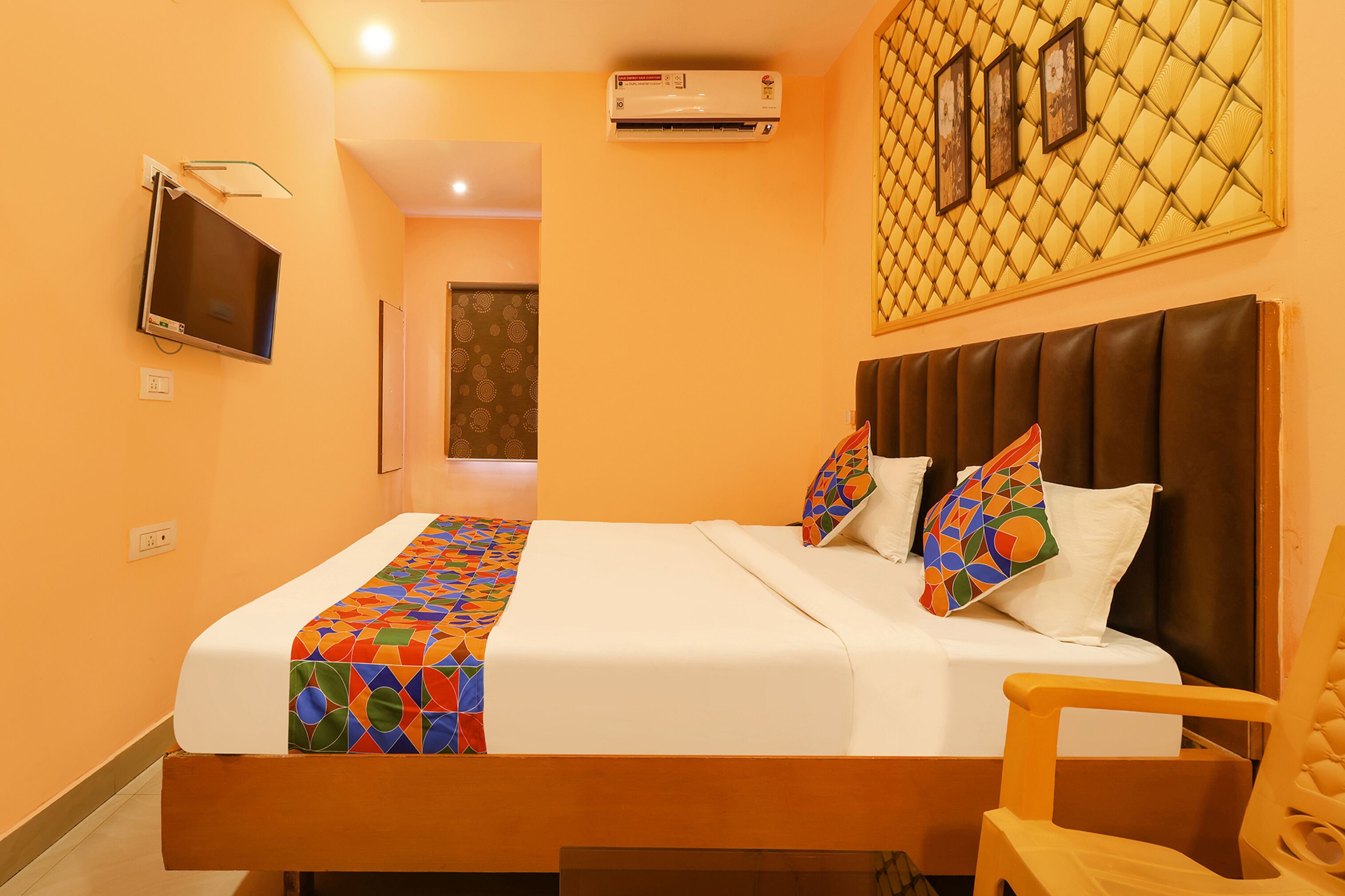 A hotel room with a bed, a TV, an air conditioner, and a decorative wall panel.