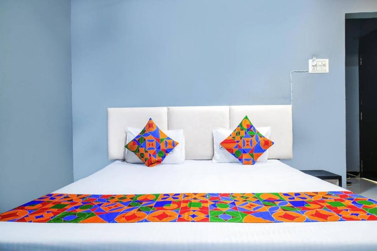 Une chambre d’hôtel avec un lit, deux oreillers, une table de chevet et une prise électrique au mur.