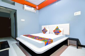 Une chambre à coucher moderne avec un lit blanc, des coussins colorés et une couvre-lit à motifs géométriques.