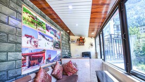 A hotel lobby with a stone wall, a wooden ceiling, and a large window offering a view of the outdoors. - FabHotel Chand Palace (Manali)