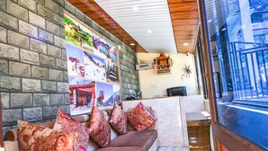 A reception area with a stone wall, a wooden ceiling, and a seating area with patterned cushions. - FabHotel Chand Palace (Manali)