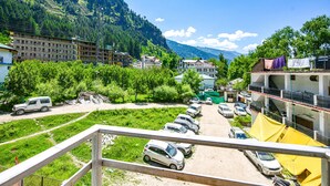 A parking lot with several cars, a building with balconies, and a mountainous backdrop. - FabHotel Chand Palace (Manali)