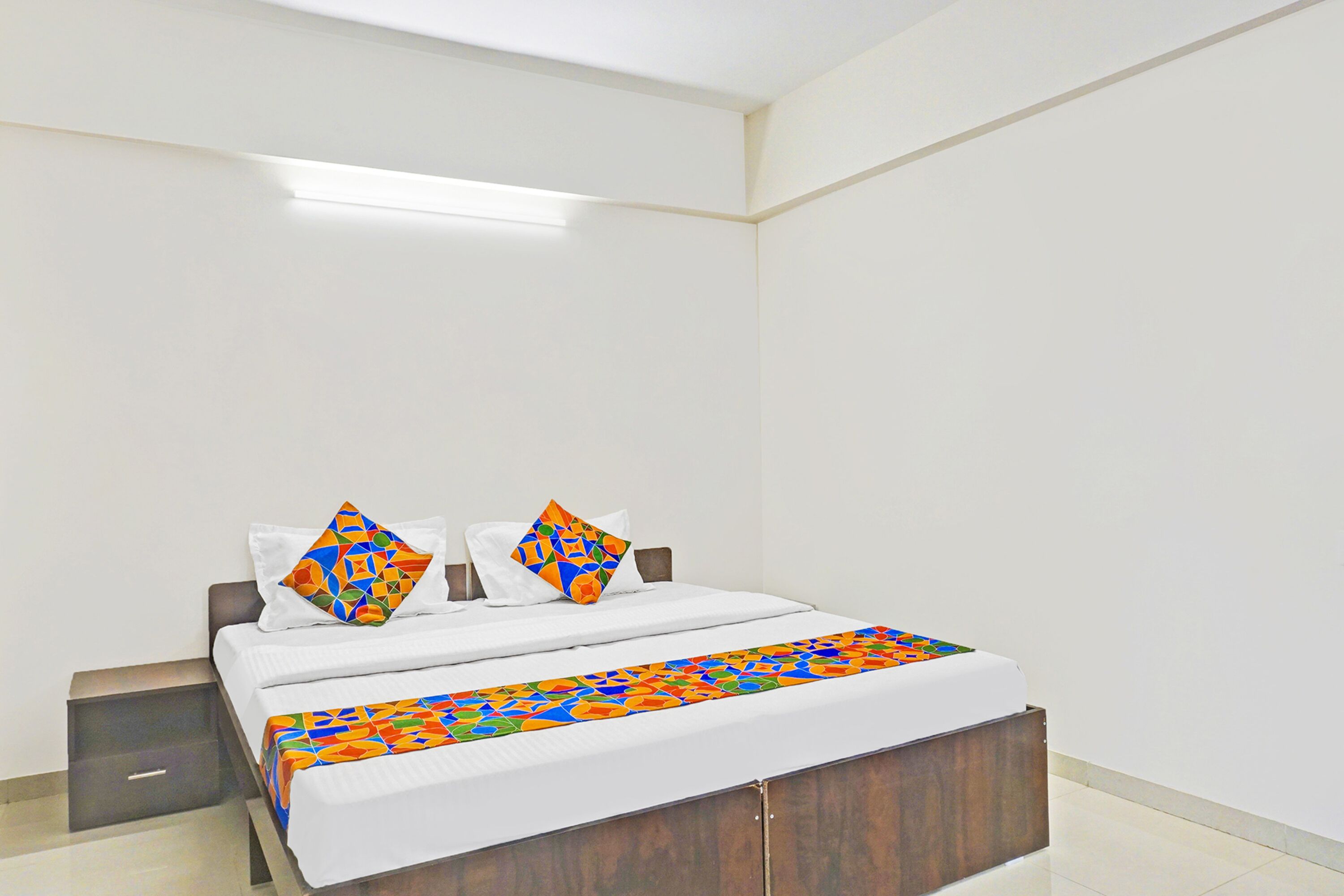 A hotel room with a bed, two pillows, a nightstand, and a wooden headboard.