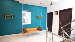 Una habitación con paredes verde azulado, un banco de madera con cojines, una hamaca colgante y una escalera con barandillas de metal.