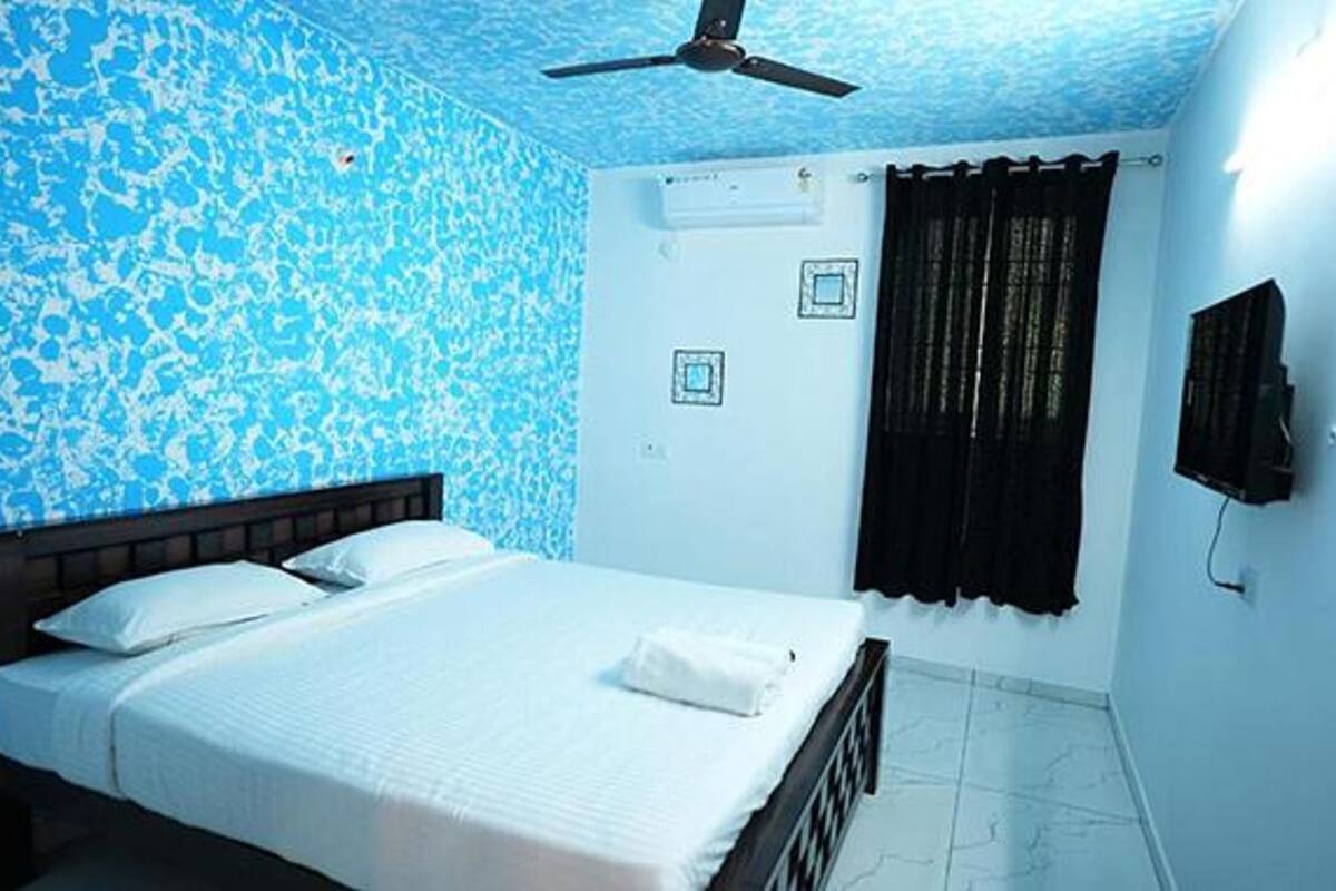 Un dormitorio con una cama, ventilador de techo, ventana con cortinas y aire acondicionado.