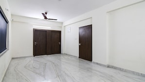 A hallway with marble flooring, two wooden doors, a ceiling fan, and recessed lighting. - FabHotel Majestic Suite (Barasat)