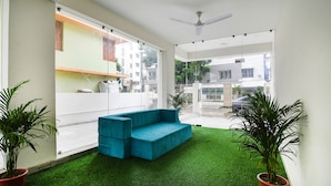 A modern living room with a teal sofa, large windows, and potted plants. - FabHotel Majestic Suite (Barasat)