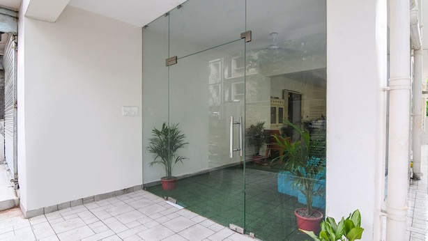A modern building entrance with a glass door, potted plants, and a tiled floor. - FabHotel Majestic Suite (Barasat)
