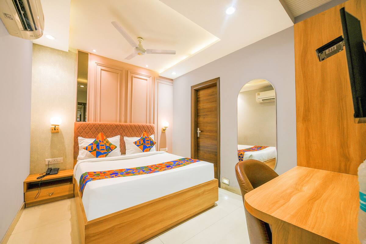 A hotel room with a large bed, a wooden desk, a chair, a mirror, and a ceiling fan.