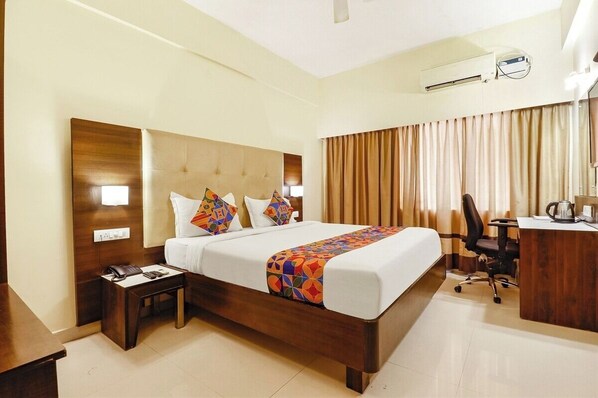 A hotel room with a wooden bed, a desk, a chair, a telephone, and an air conditioning unit. - Hotel Magaji Comfort Inn (Bengaluru)