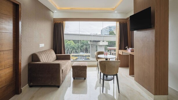 Una habitación de hotel moderna con sofá, reposapiés, mesa de comedor, sillas y televisor montado en la pared.