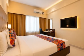 A hotel room with a bed, a desk, a chair, an air conditioning unit, and a television. - Hotel Magaji Comfort Inn (Bengaluru)