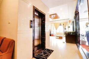 An interior hallway with a marble elevator, a seating area with a sofa, and a window with curtains. - Hotel Magaji Comfort Inn (Bengaluru)