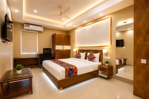 A modern hotel room with a large bed, bedside tables, a desk, a chair, an air conditioning unit, a ceiling fan, and a television. - Hotel Magaji Comfort Inn (Bengaluru)