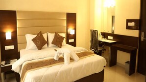Habitación de hotel con una cama grande, dos mesitas de noche, un escritorio, una silla, un espejo y un cesto de basura.
