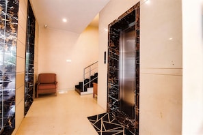 A modern elevator with a marble finish, a chair, and a staircase with a geometric floor design. - Hotel Magaji Comfort Inn (Bengaluru)
