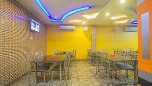 Une salle de conférence avec un mur en briques, des murs jaunes et un sol carrelé. Des tables et des chaises y sont disposées pour les réunions.