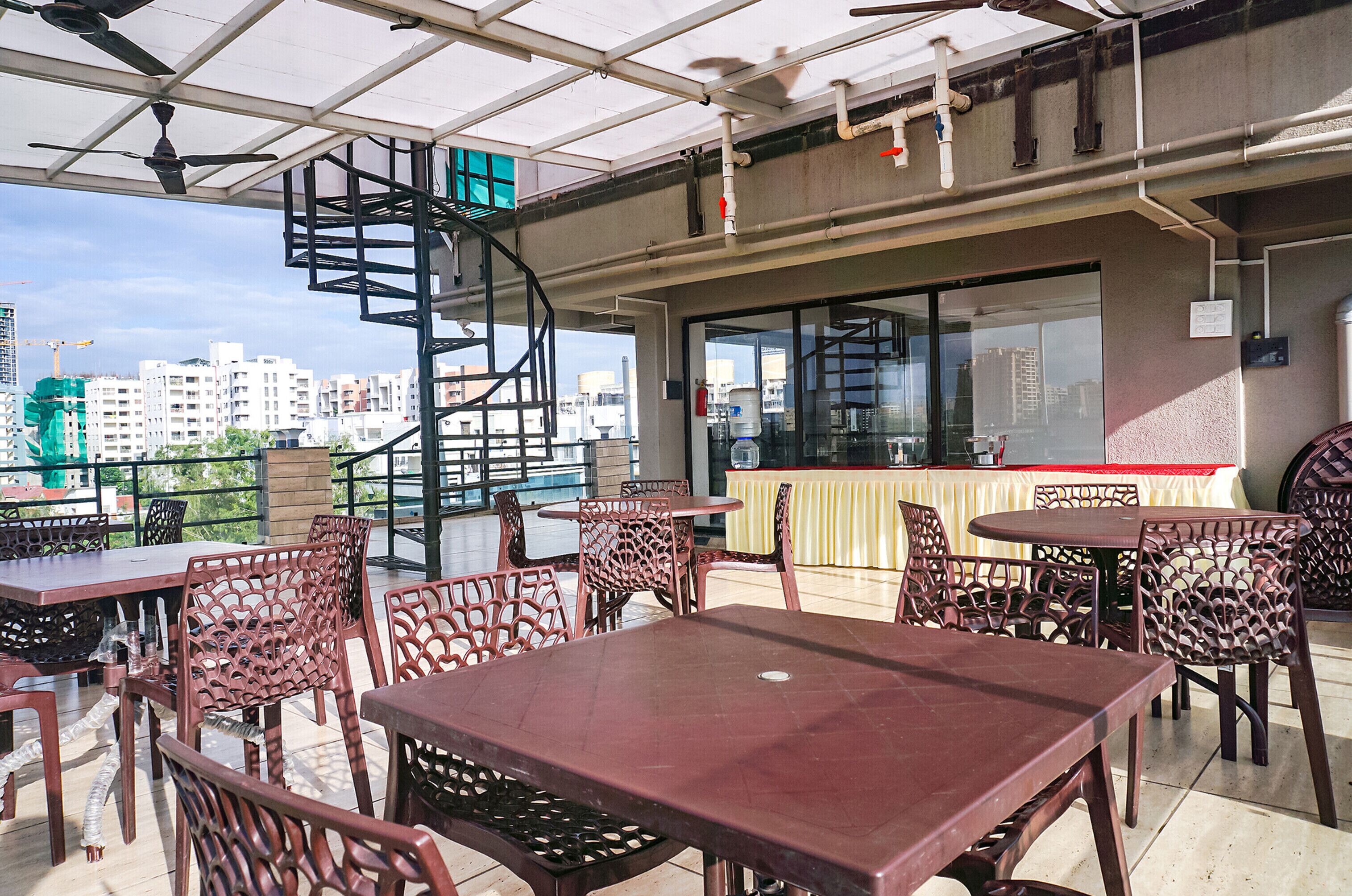 An outdoor dining area with multiple tables and chairs, a spiral staircase, and a view of the cityscape in the background.