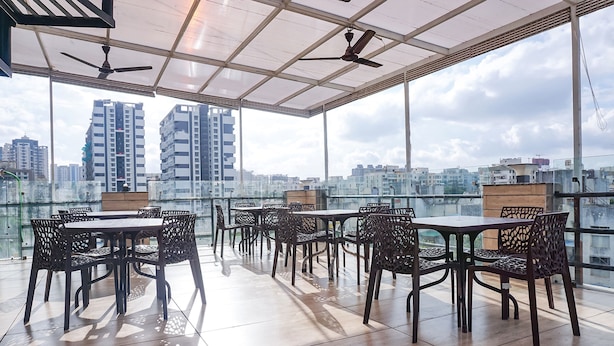 A rooftop terrace with a table and chairs, a ceiling fan, and a view of city buildings. - FabHotel Atithi Regency (Pune)