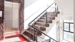 A modern elevator with a metallic finish, a staircase with a glass railing, and a red carpet leading to the elevator. - FabHotel Atithi Regency (Pune)