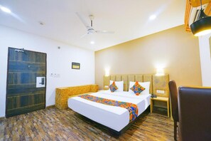 A hotel room with a large bed, a ceiling fan, a nightstand, and a chair. - FabHotel The Residency 44 Noida (Noida)