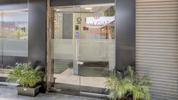 The entrance to Hotel Golden Sands Inn with a glass door, a clock, and a sign indicating rooms are available. - FabExpress Golden Sands inn (Mumbai)